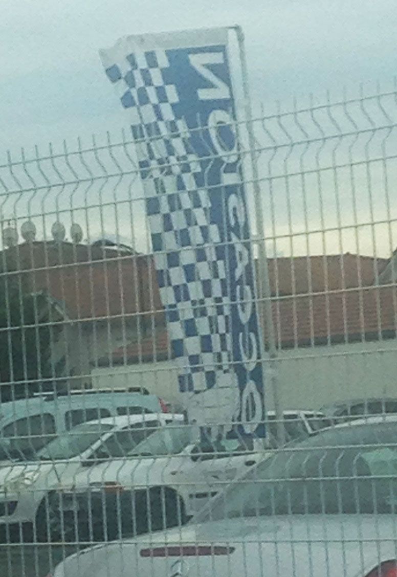 Drapeau OCCASION ECO damier bleu 220x95 cm sur mât télescopique 4 mètres dans petit parc automobile garage indépendant